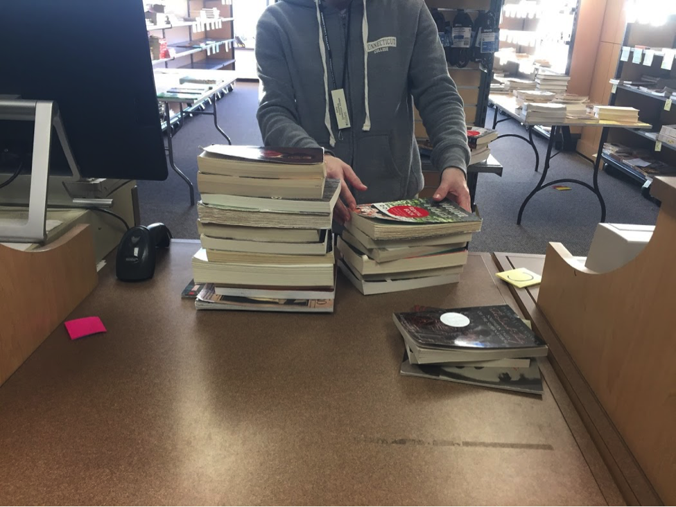 A student stands behind a pile of books stacked on a counter.