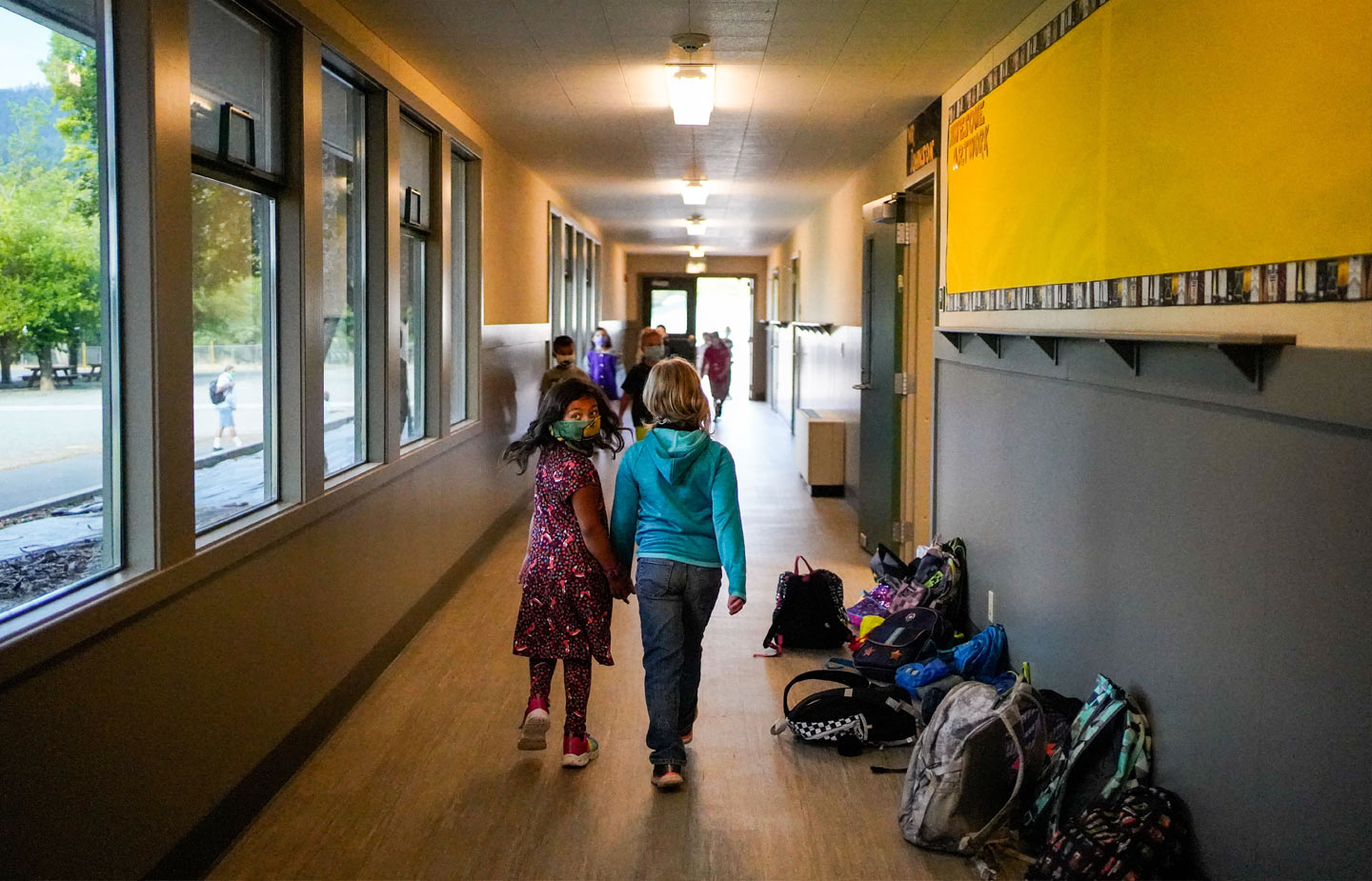 two young children walking down a school laundry wearing masks