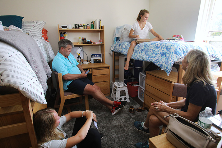 A student sits on her raised bed as her family looks on.