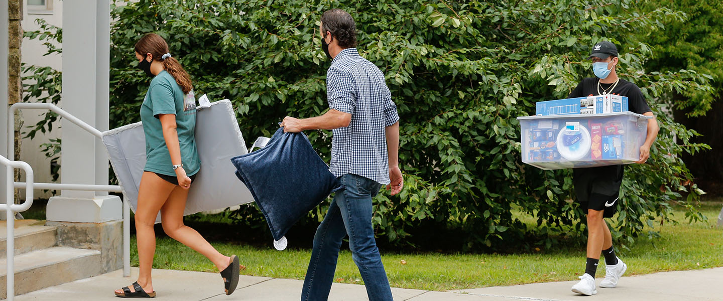 Students and their family members carry belongings into a dorm.