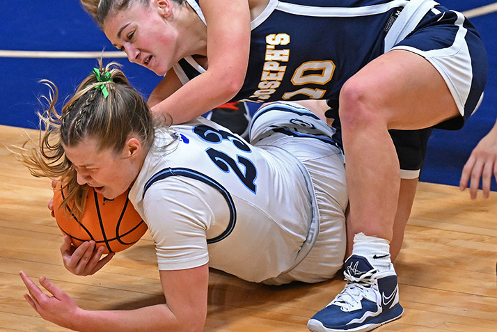 Two players wrestle for the basketball on the floor of the court.