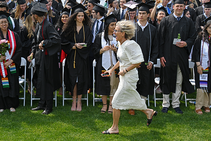 A smiling person jogs past graduates