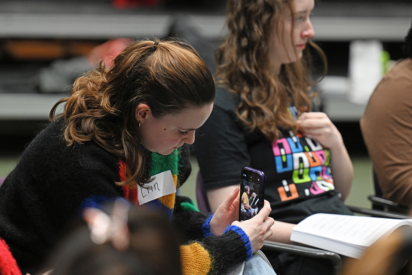 A student take a photo with a smart phone of another during vocal rehearsal.