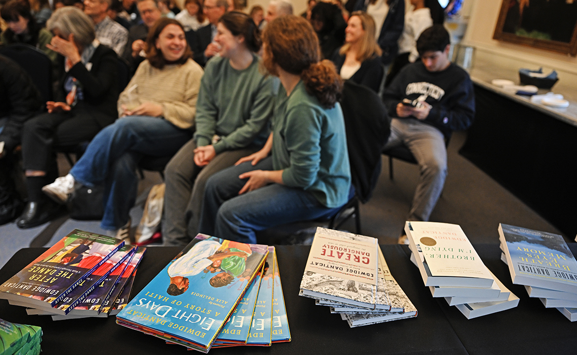 A table featuring books by Edwidge Danticat in the foreground while the audience waits for the Symposium to begin.