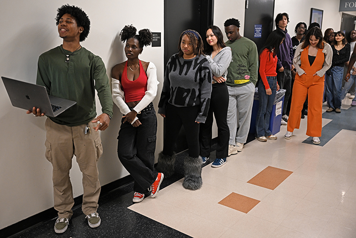 a student with laptop computer in hand gives instructions to students practicing fashion show walking