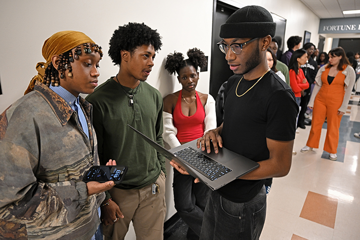 three students huddle around a laptop computer