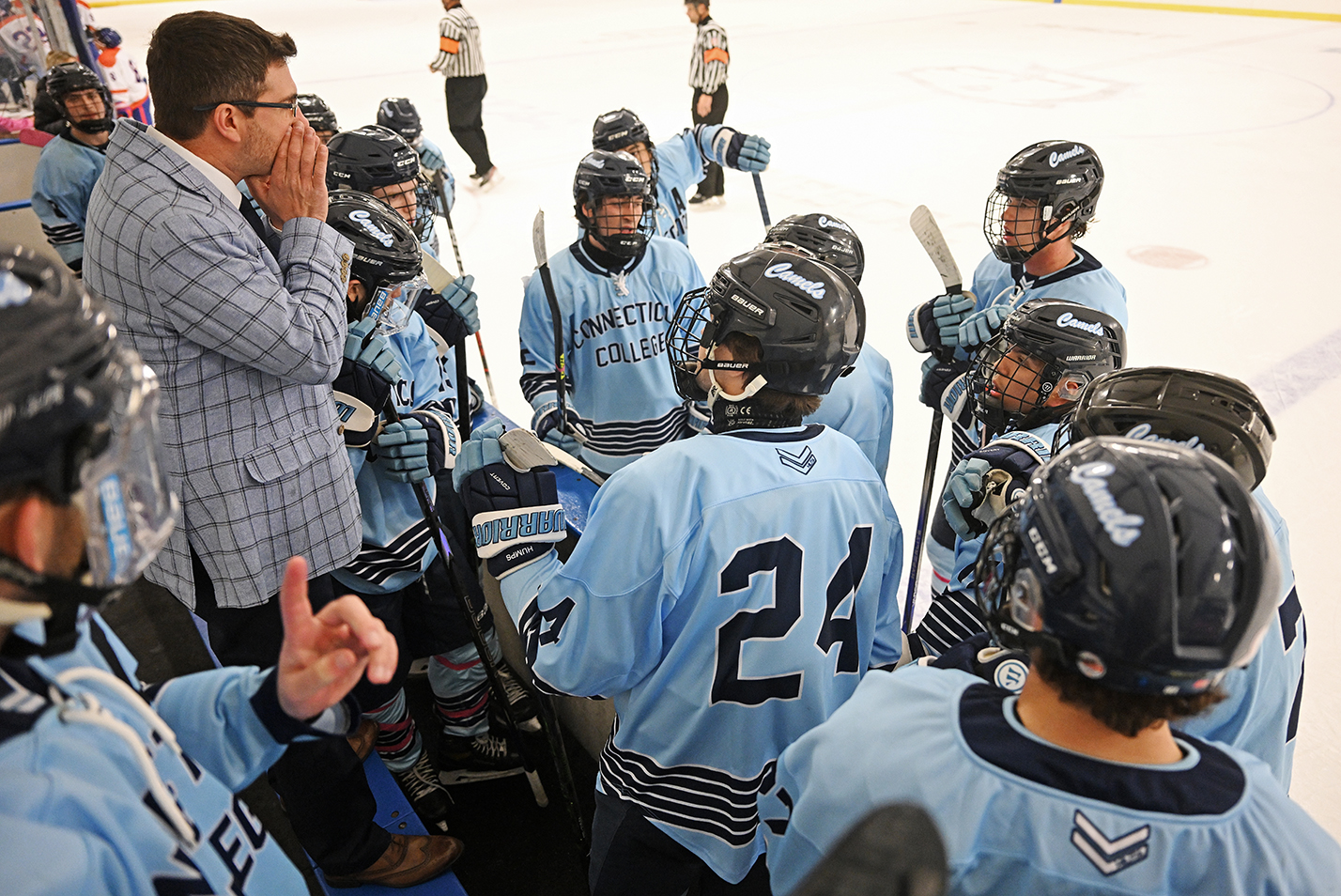 A hockey coach huddles with his players at the bench.