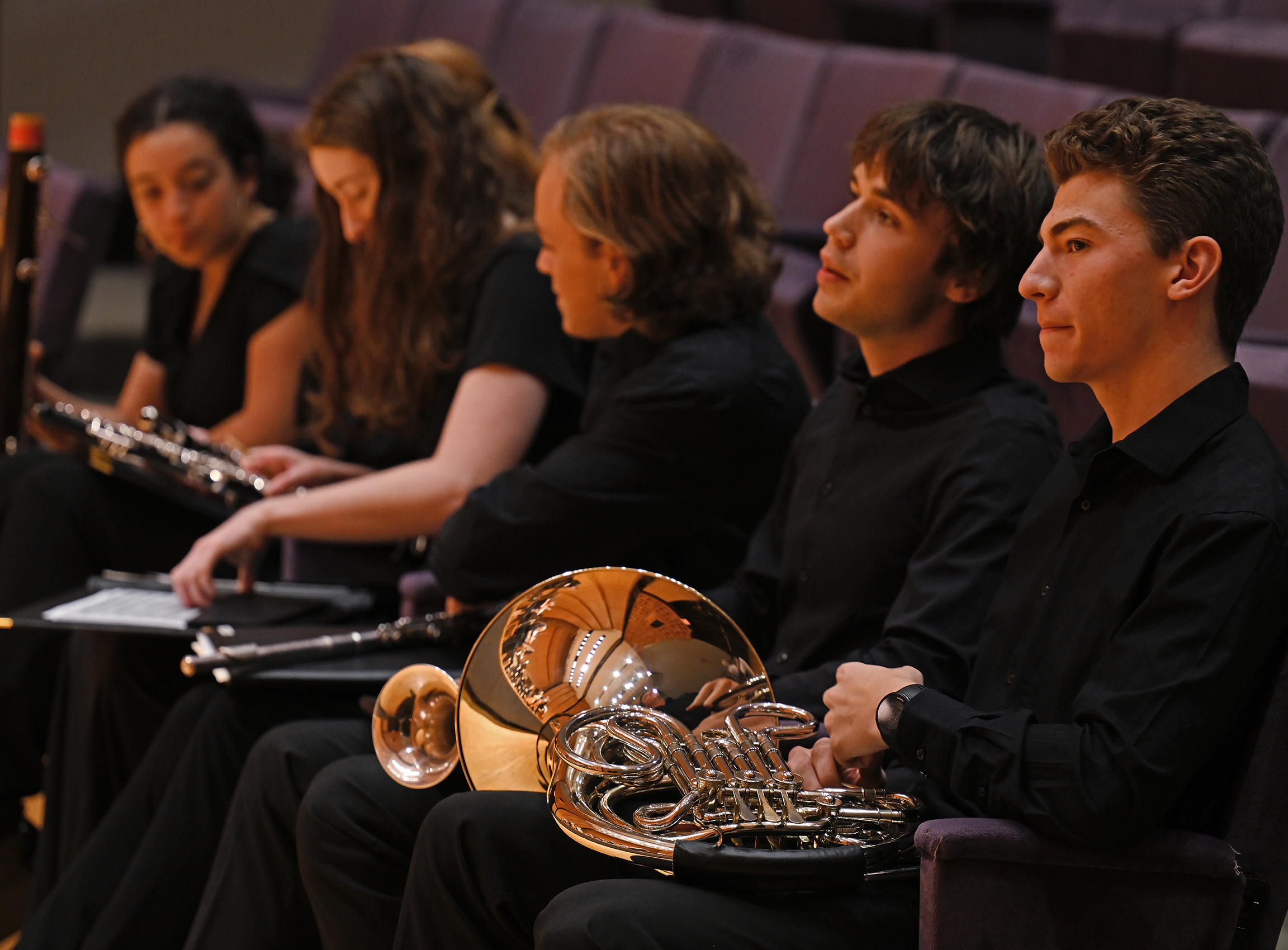 Student musicians sit in the audience with their instruments awaiting their turn on stage.