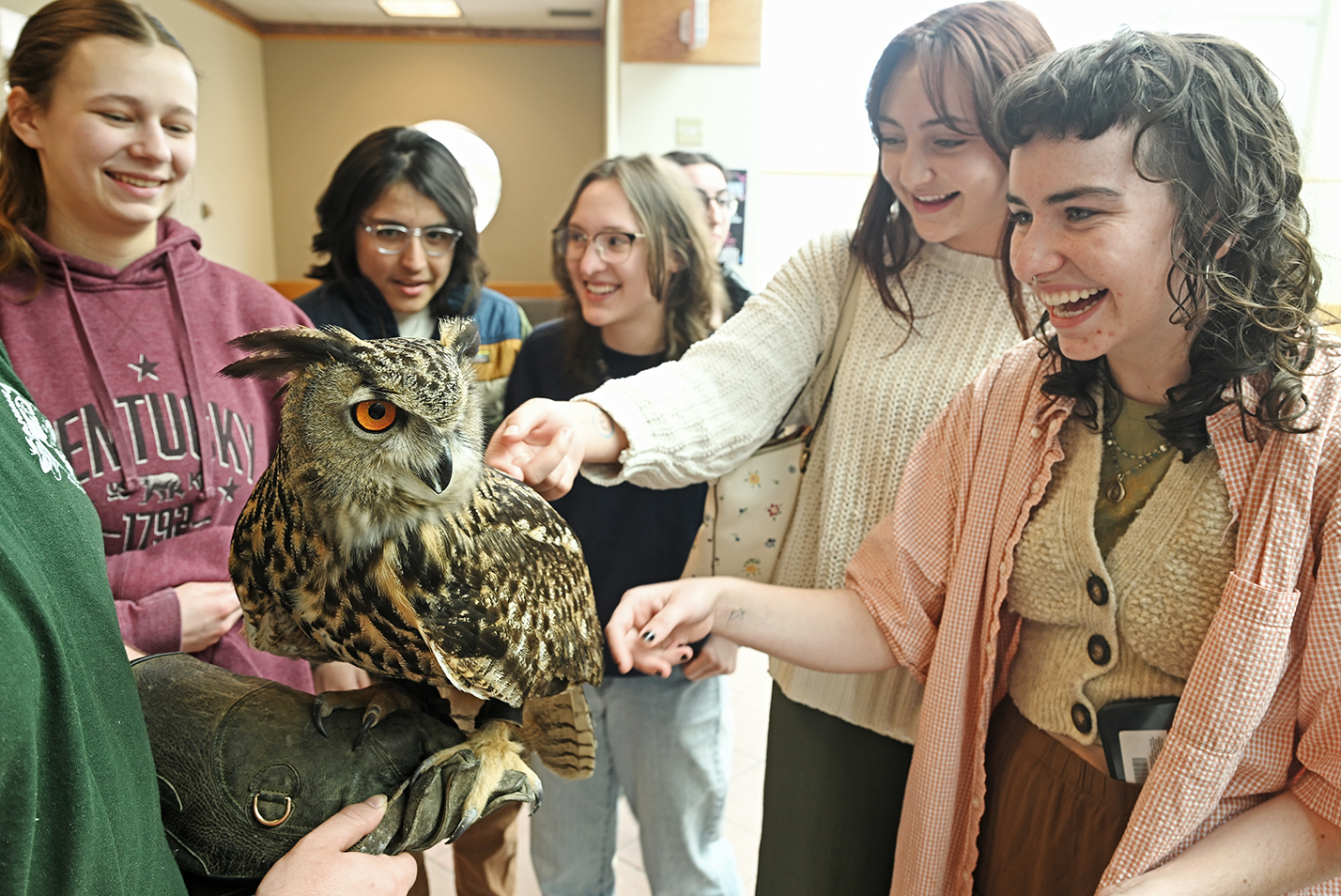 College students pet an owl with large orange eyes.