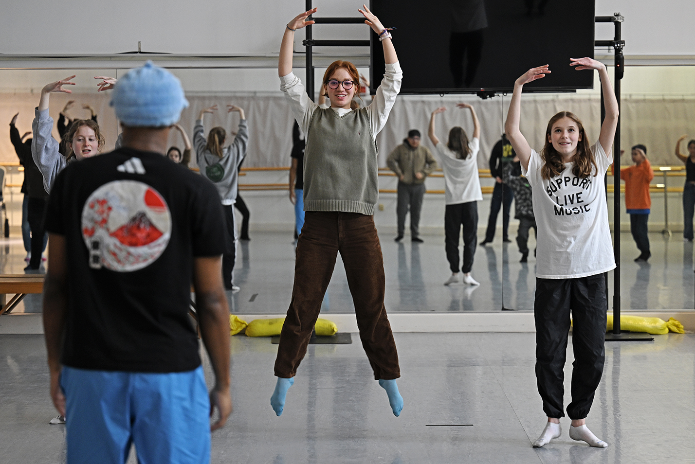 Three student dancers demonstrate dance moves to a dance studio full of middle graders reflected in a mirrored wall.