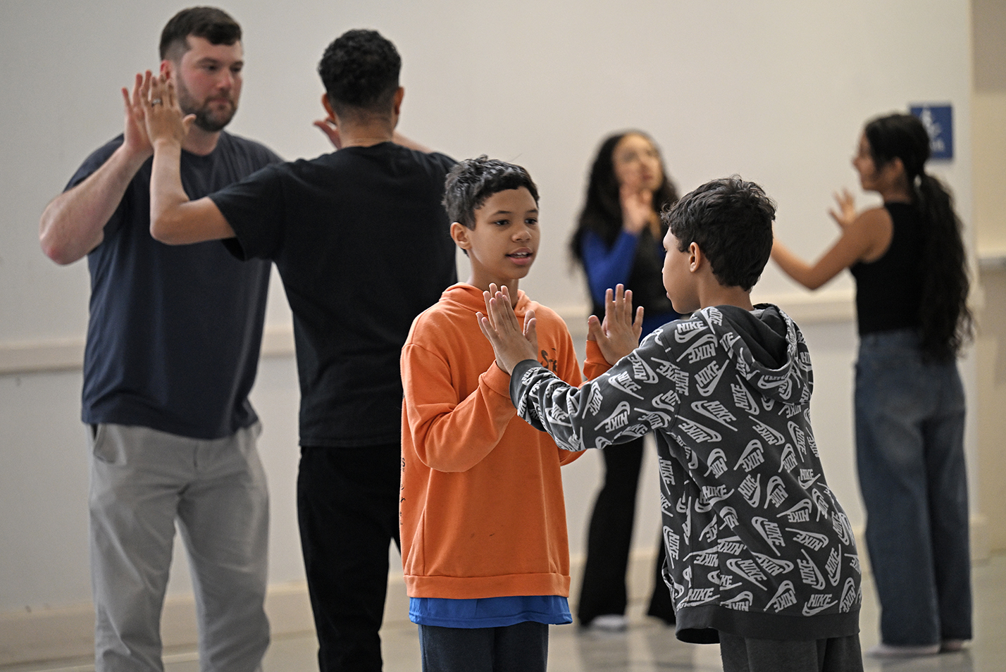 Middle school students and their teachers practice dance moves during a dance workshop in a college dance studio.
