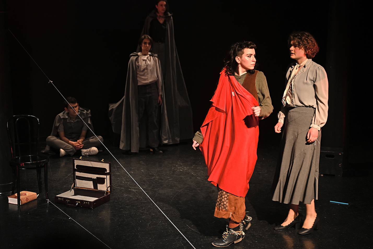 Actors in a student play production act in a scene in a black box theater.