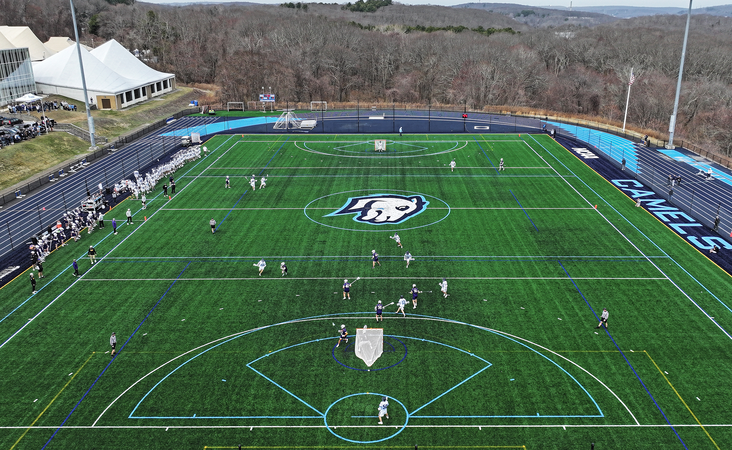 Men's lacrosse players take to a newly renovated turf field as seen from the air.