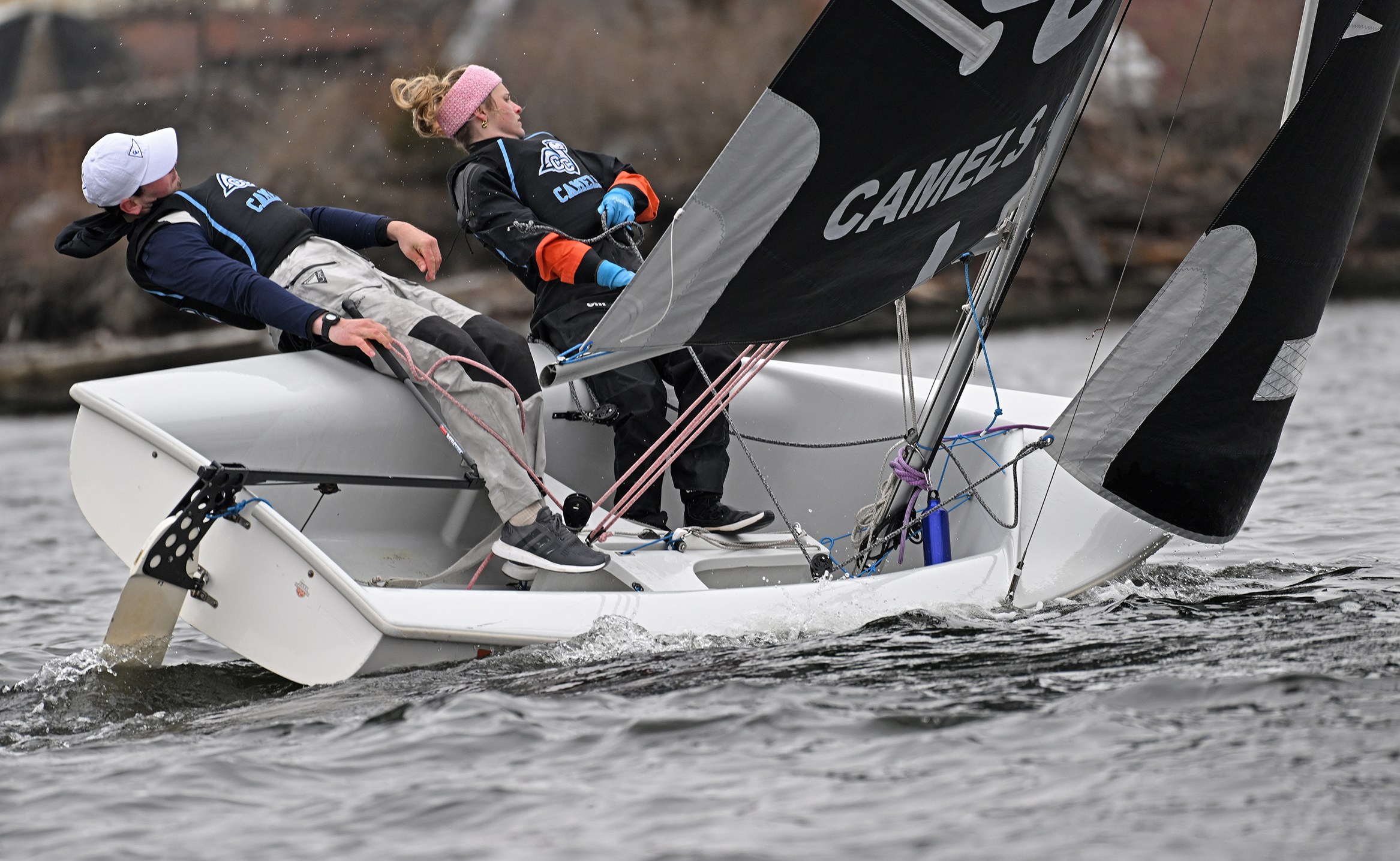 A pair of collegiate sailors lay out off the port side as they execute a turn during a race.