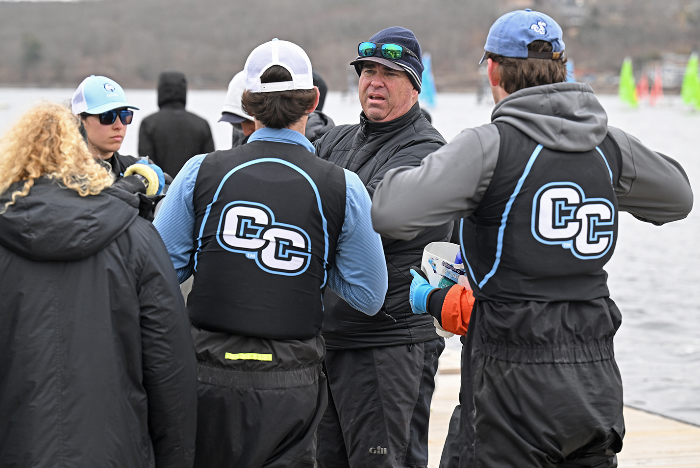 A college sailing coach meets with his team on the dock.