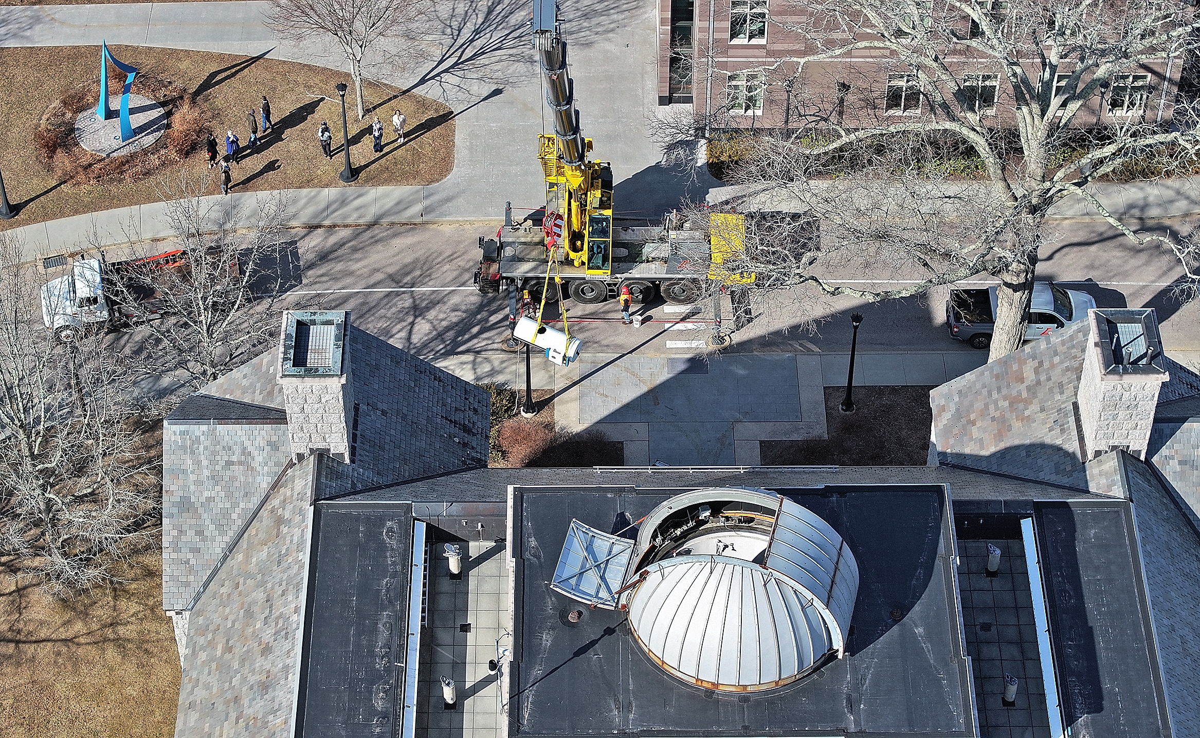 Seen from the air, a crane lifts a telescope from a rooftop observatory.